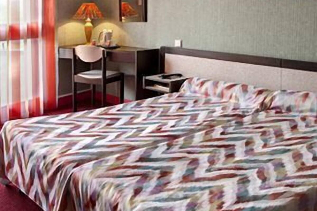 A hotel room with a bed, a desk, a chair, and a lamp.