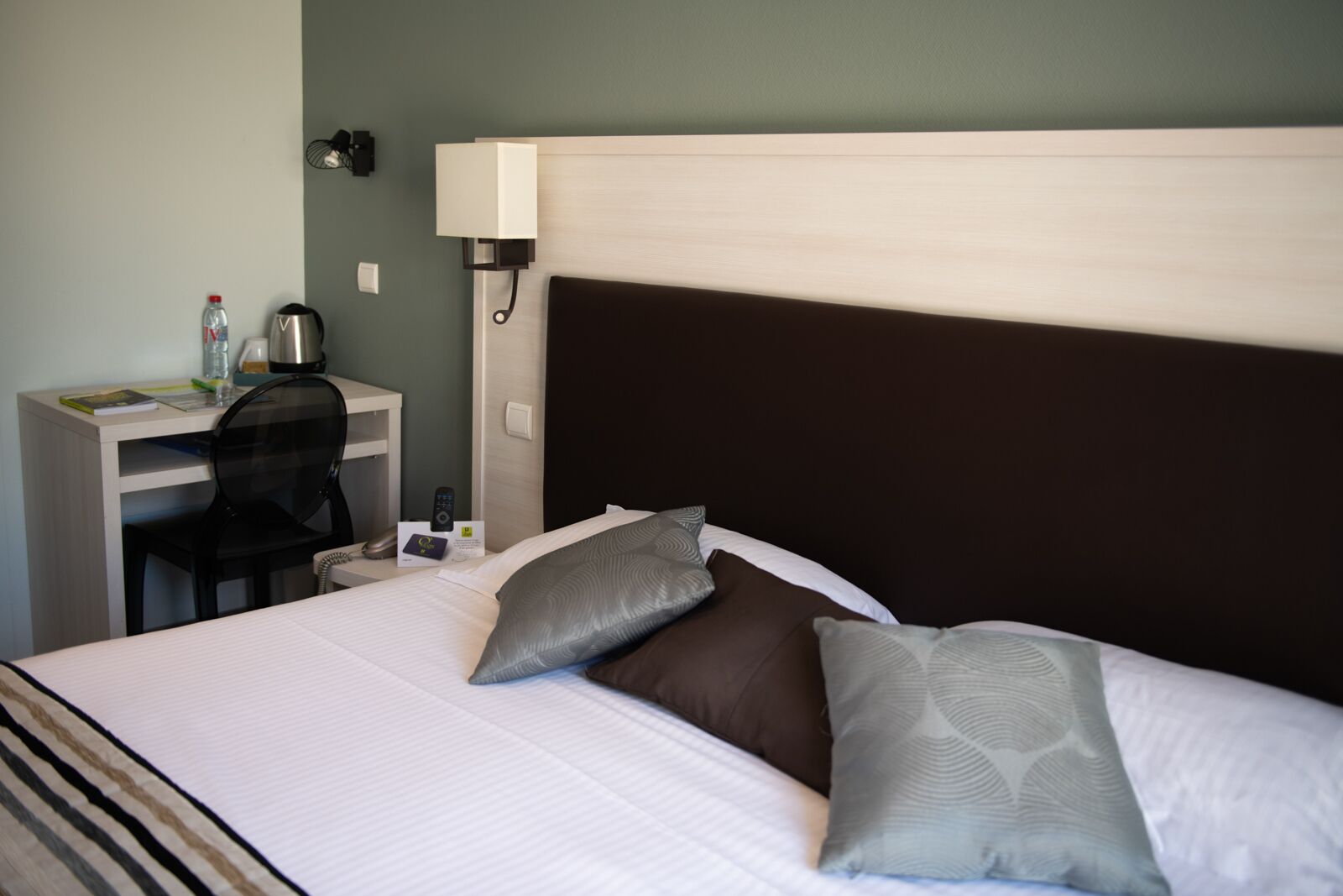 Une chambre d’hôtel équipée d’un lit, d’un bureau, d’une chaise, d’une lampe et d’un téléphone fixé au mur.