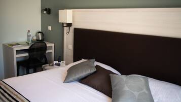 Une chambre d’hôtel équipée d’un lit, d’un bureau, d’une chaise, d’une lampe et d’un téléphone fixé au mur.