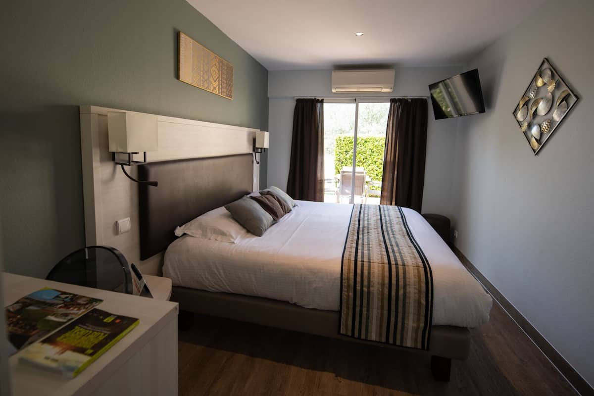 A hotel room with a bed, bedside table, and a TV mounted on the wall.