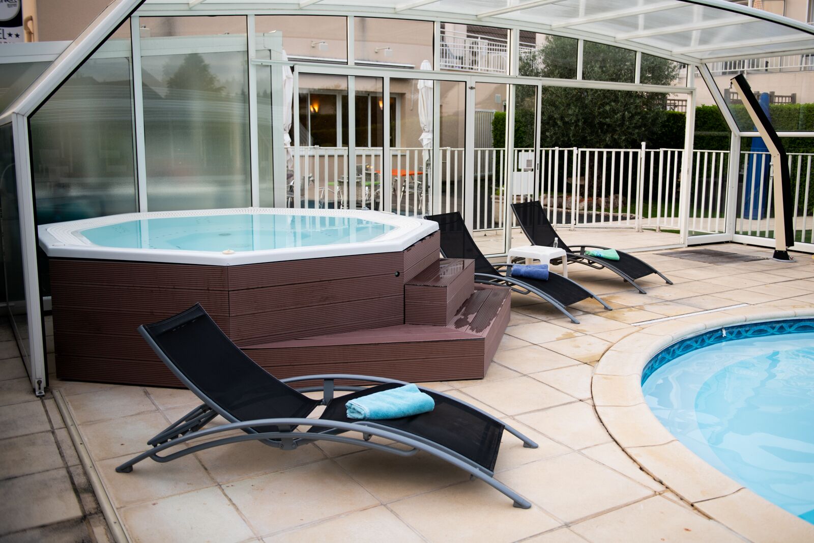 A covered outdoor swimming pool area with a hot tub and lounge chairs.