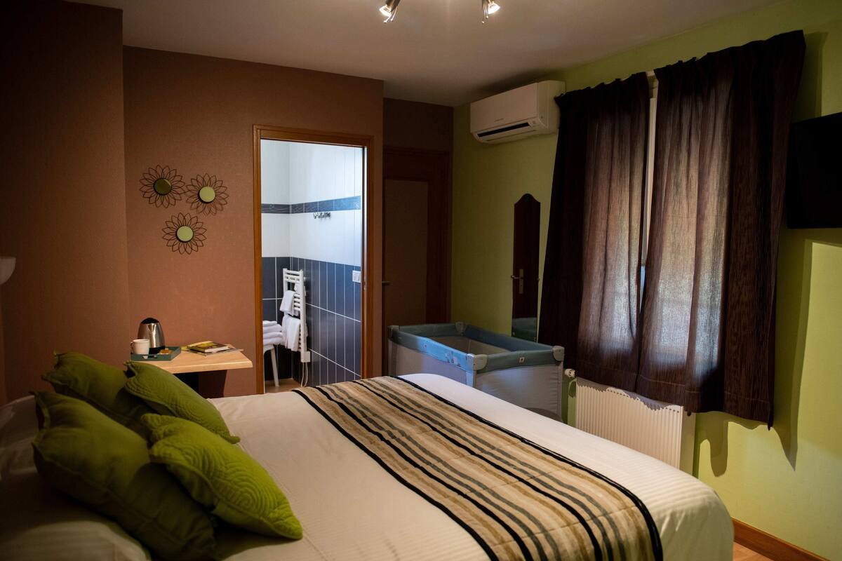 A hotel room with a bed, a desk, a radiator, and a window with curtains.