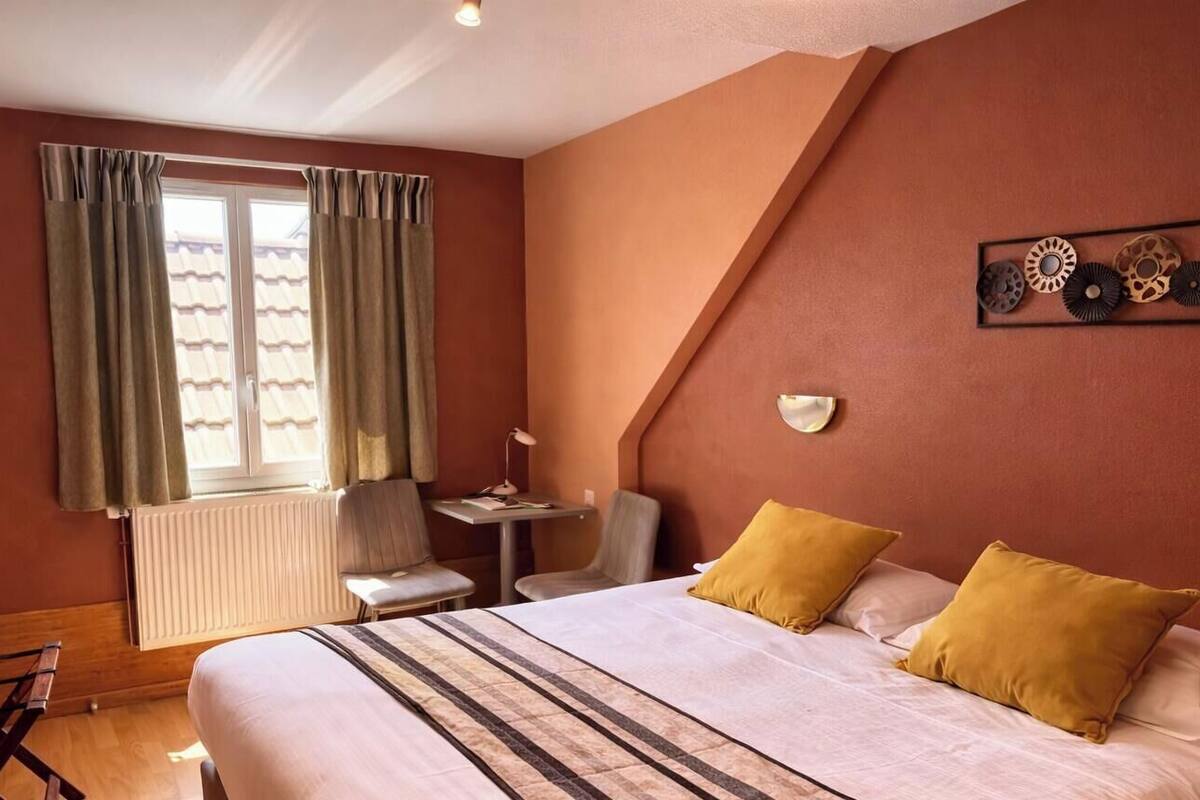 A bedroom with a bed, two chairs, a small table, a TV, and a window with curtains.
