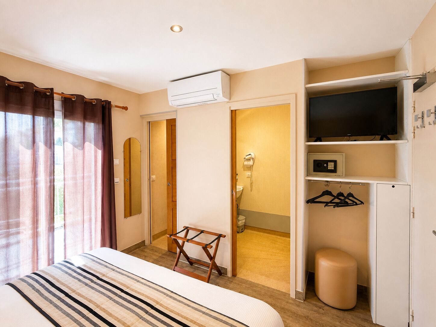 A hotel room with a bed, a wardrobe, a television, a mirror, and a bathroom visible through an open door.