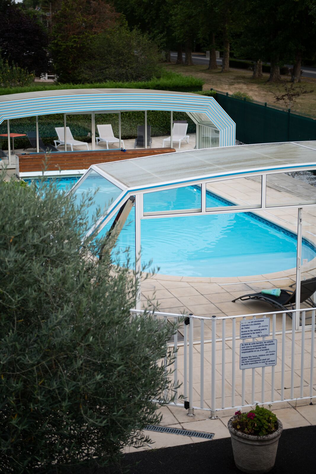 Una piscina con area prendisole coperta, sedie a sdraio e un cartello di sicurezza.