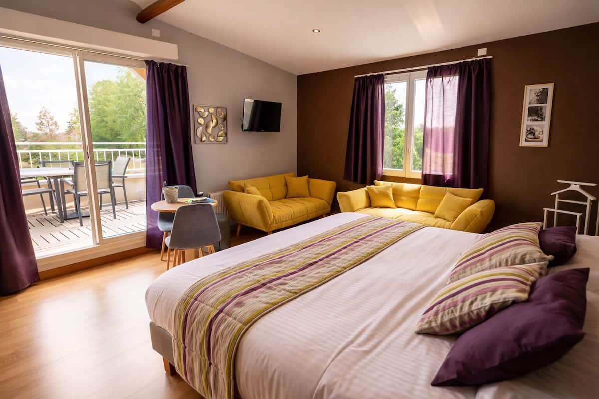 A bedroom with a large bed, a sofa, a TV, and a balcony with outdoor furniture.