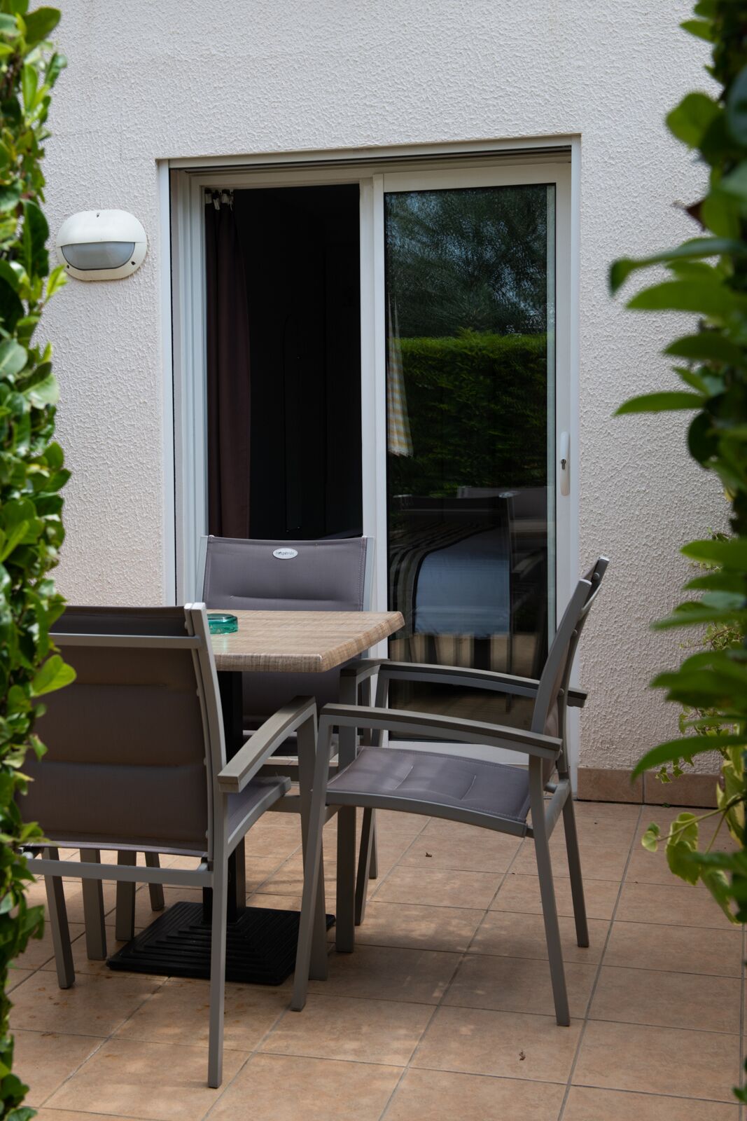 Un espace patio extérieur avec une table et des chaises, une porte-fenêtre coulissante et un mur blanc à texture.