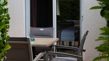Un espace patio extérieur avec une table et des chaises, une porte-fenêtre coulissante et un mur blanc à texture.