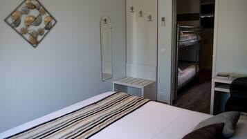 A bedroom with a bed, a bedside table, a mirror, a wardrobe, and a bunk bed in the background.