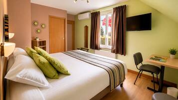 Een slaapkamer met een bed, een bureau, een stoel, een televisie en een raam met gordijnen.