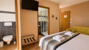 Una habitación de hotel con cama, televisión, ducha y baño.