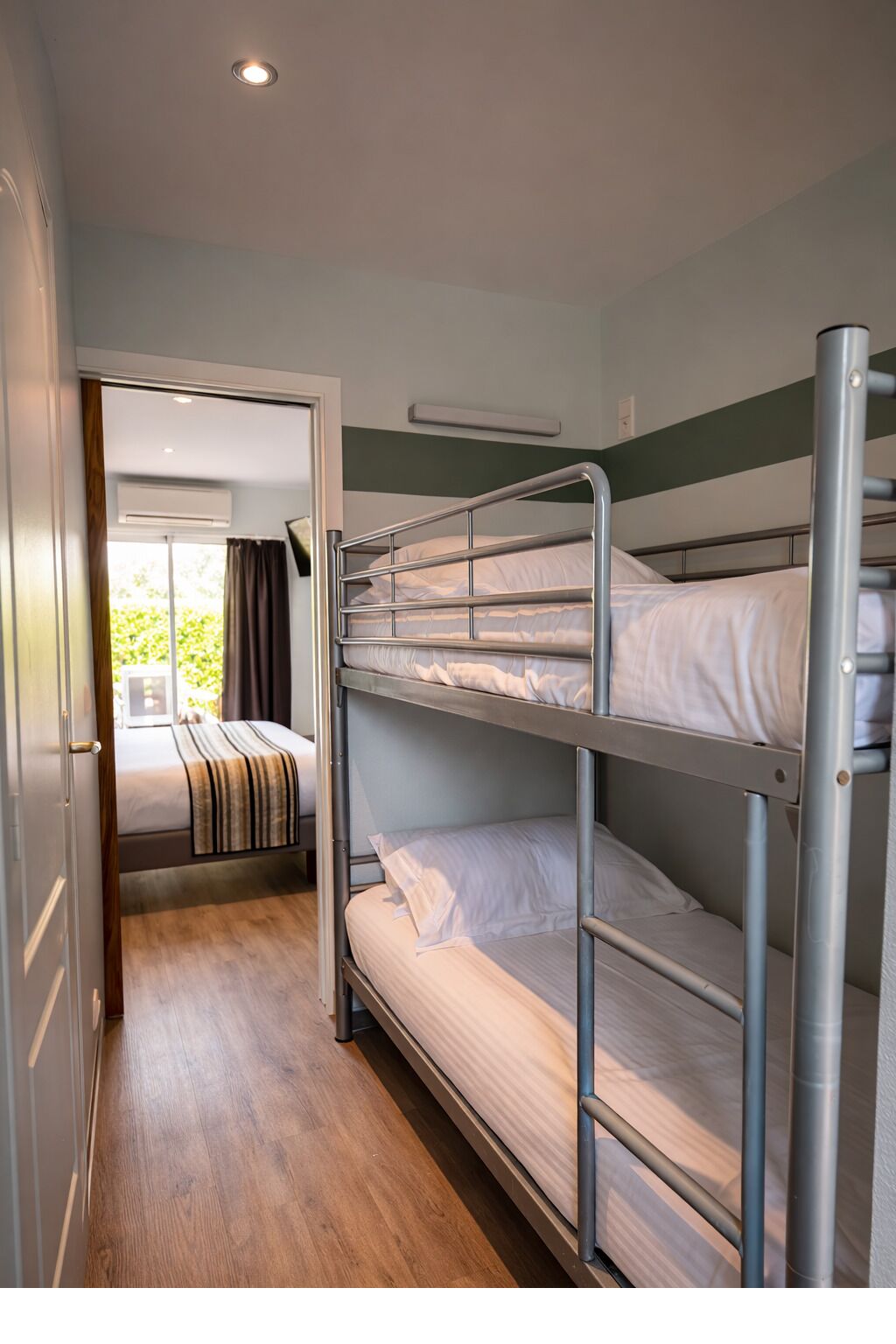 A bunk bed room with a wooden floor, a door leading to a balcony, and a window.