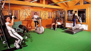 Et fitnessrum med træbjælker, grøn gulvbelægning og forskellig træningsudstyr.