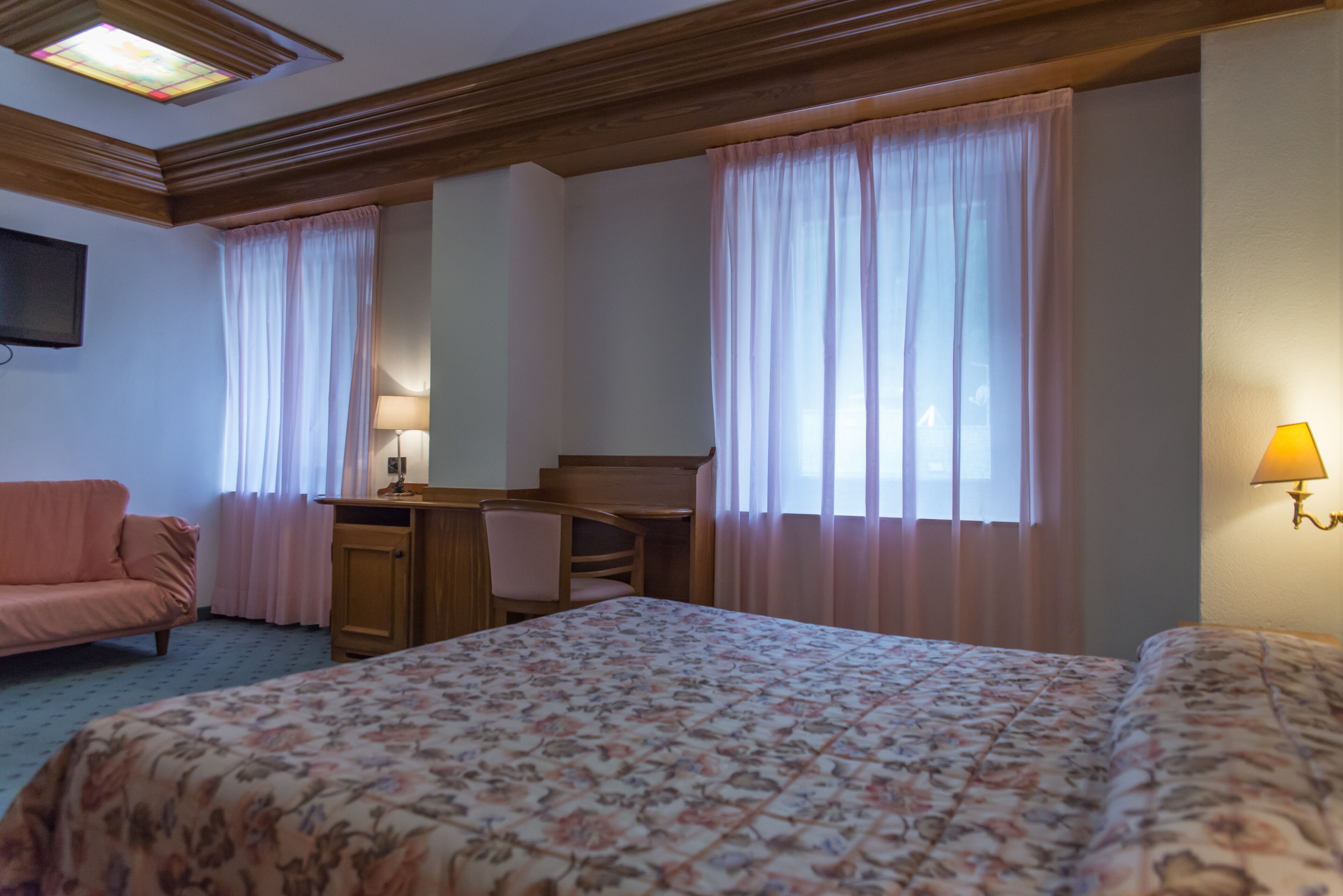 A hotel room with a bed, a desk, a chair, a sofa, and a TV on the wall.