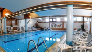 En indendørs swimmingpool med liggestole og et træloft.