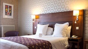 Ein Hotelzimmer mit einem großen Bett, zwei Nachttischlampen, einem Telefon und einem Sessel.