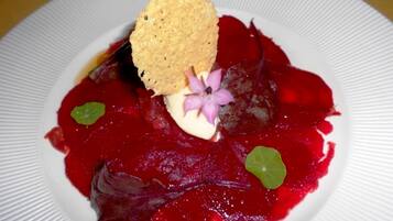 Une assiette blanche contenant un plat à base de betterave, agrémenté d’une fleur et d’un biscuit salé.