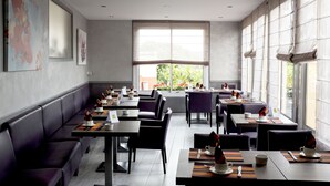 Ein modernes Restaurant mit langen Gemeinschaftstischen und Sitzecken, großen Fenstern mit Jalousien sowie Kunstwerken an den Wänden.