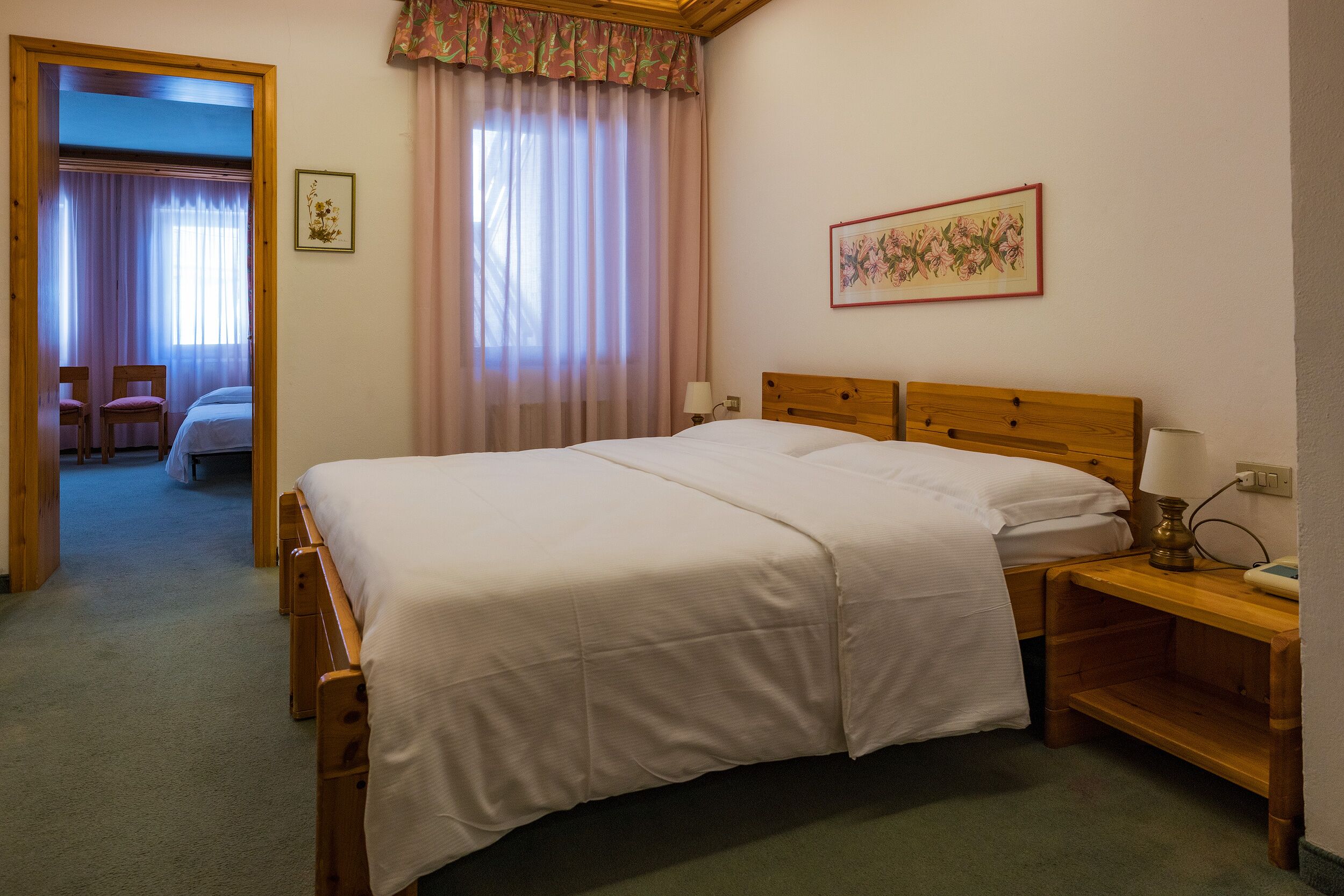 A bedroom with a large bed, wooden headboard, bedside tables, and a door leading to another room.