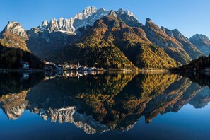 Un lago tranquilo que refleja montañas y un pequeño pueblo con edificios a lo largo de la orilla.