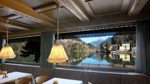 A dining area with tables and chairs, a view of a lake, and a mountain in the background.