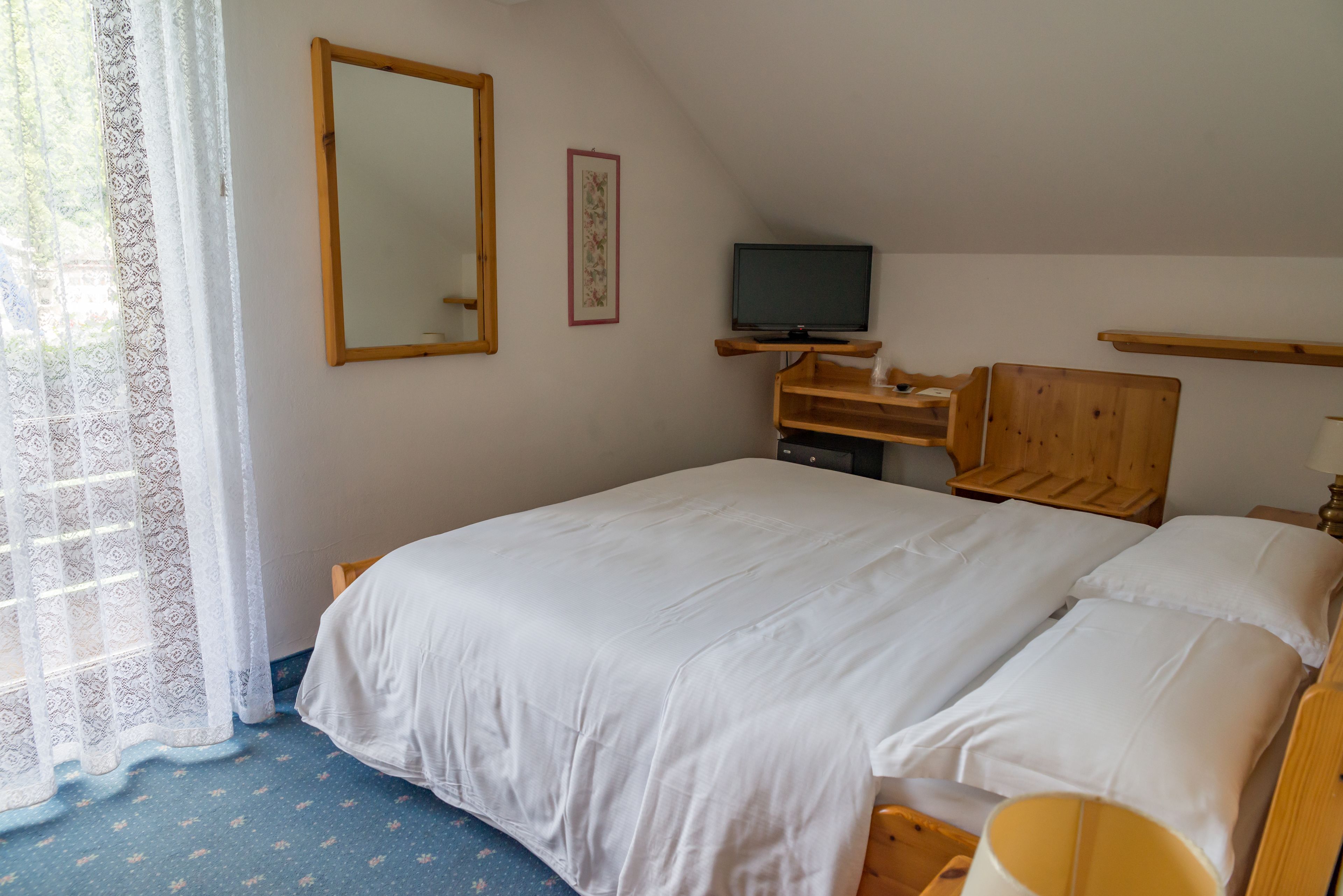 A neatly arranged bedroom with a bed, a television on a wooden stand, a mirror, and a framed picture on the wall.