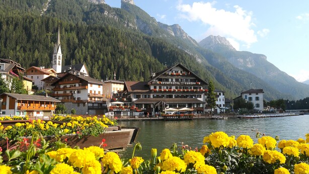 A hotel with a restaurant and bar, located by a lake with mountains in the background.