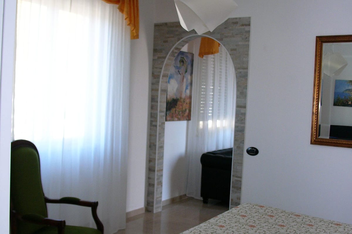 A hotel room with a bed, a chair, a desk, a lamp, and a painting on the wall.