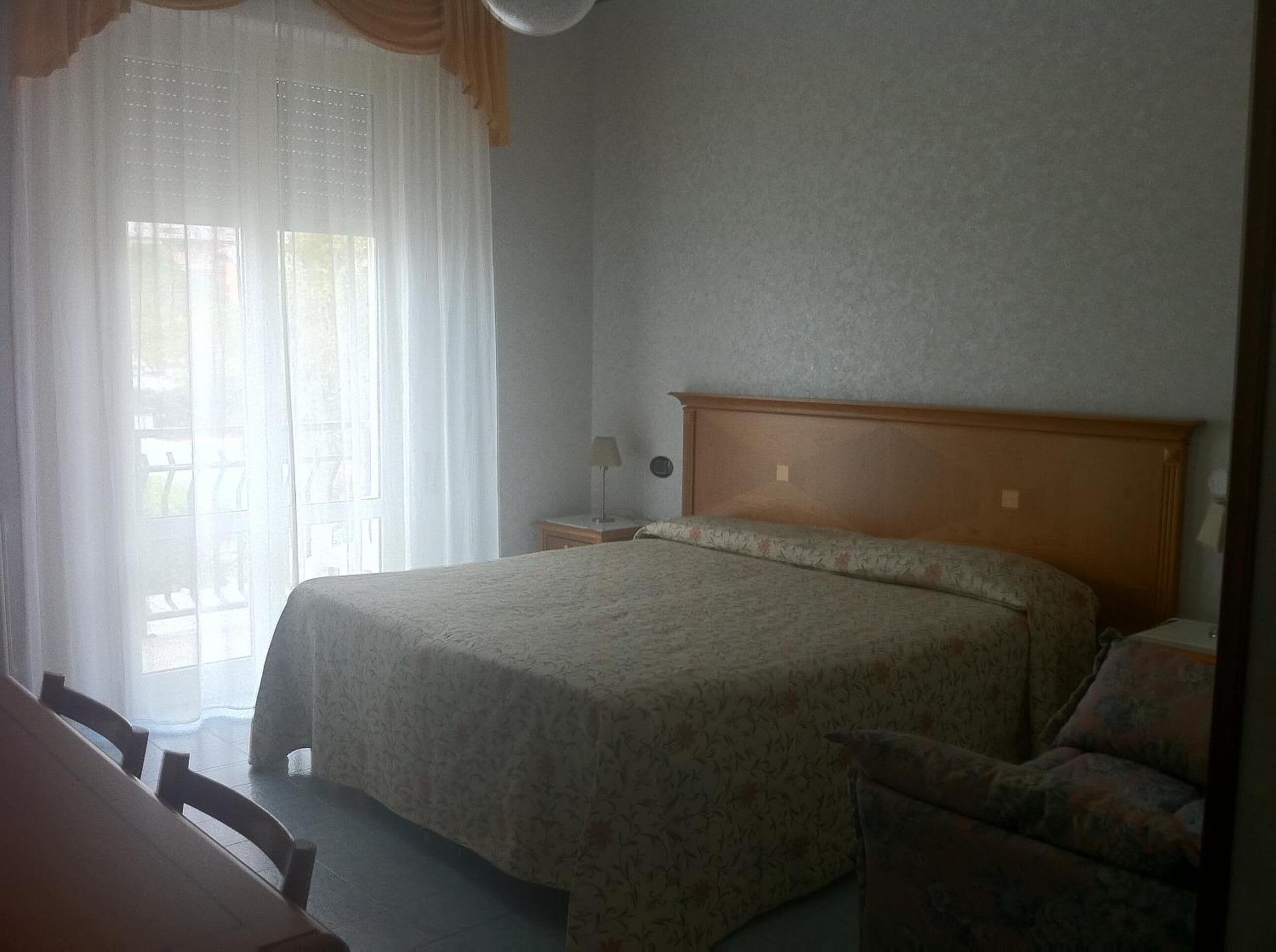 A bedroom with a bed, a chair, a nightstand, and a window with curtains.