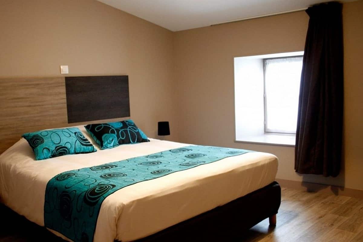 A bedroom with a bed, a window, and a nightstand with a lamp.