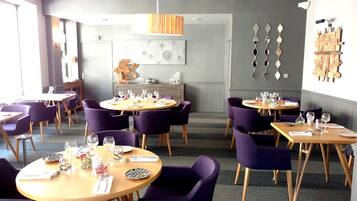 A restaurant with round tables and purple chairs, featuring a modern interior with a wooden ceiling and decorative wall art.