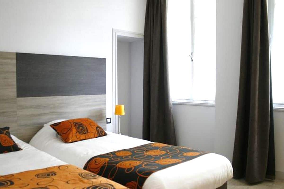 A hotel room with two beds, a large window with curtains, and a modern headboard.