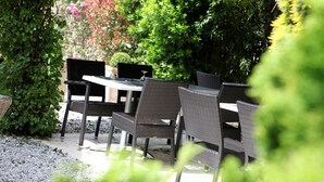 An outdoor seating area with wicker chairs and a table, surrounded by greenery.
