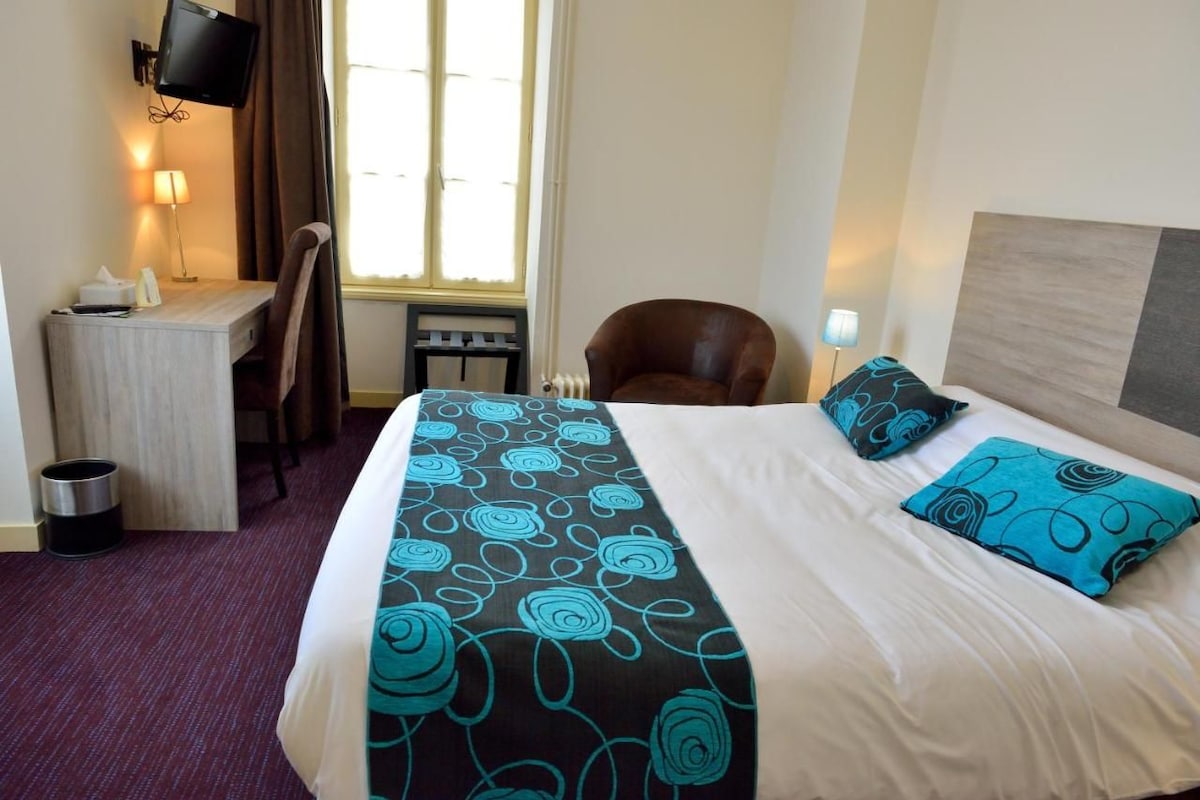 A hotel room with a bed, a desk, a chair, a TV, and a window.
