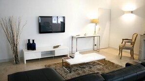 A modern living room with a flat-screen TV mounted on the wall, a white console table, a coffee table, a sofa, and a chair.