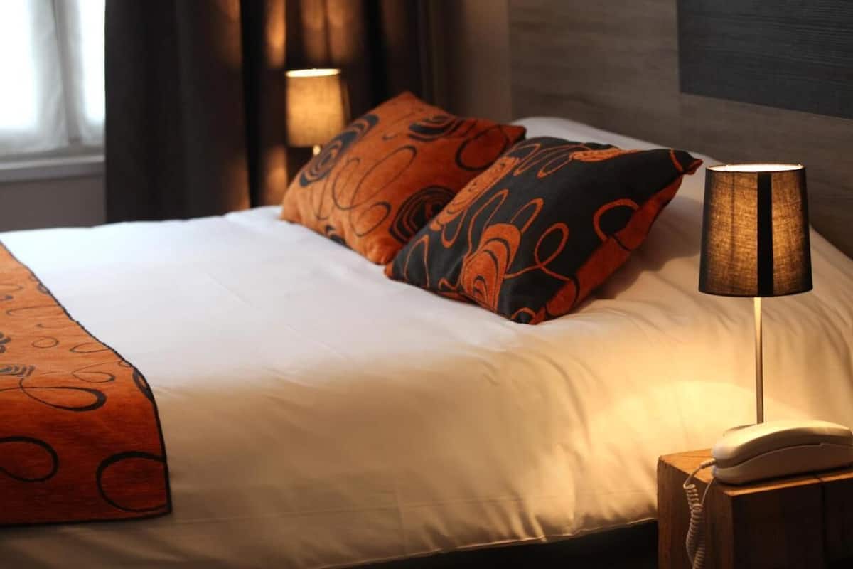 A neatly made bed with patterned pillows, a bedside lamp, and a telephone on a wooden nightstand.