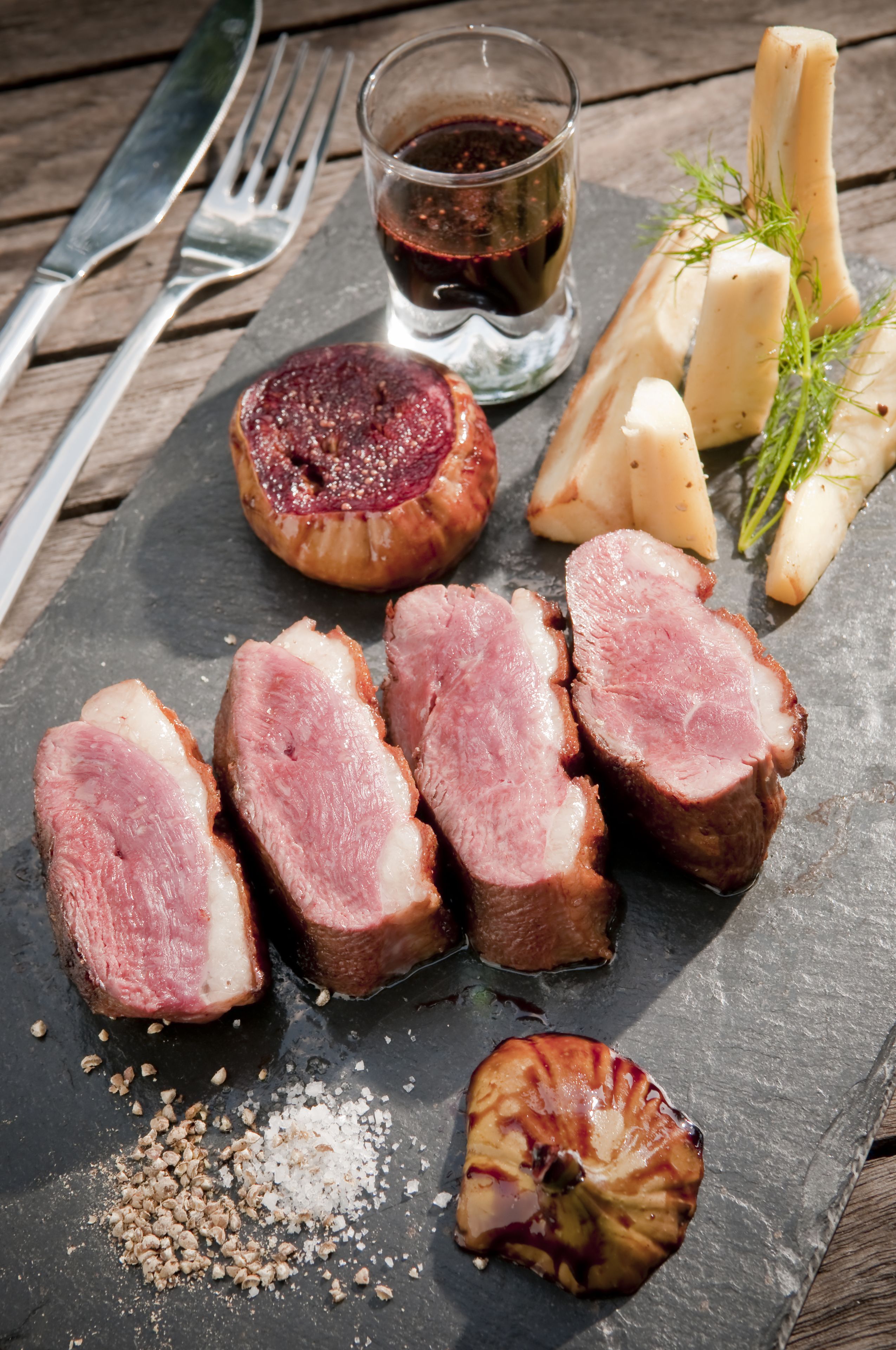 Une planche de service en ardoise, garnie de tranches de viande, d’oignons marinés et de fromage.