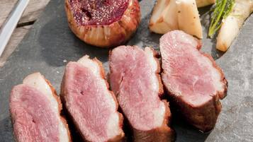 Une planche de service en ardoise, garnie de tranches de viande, d’oignons marinés et de fromage.