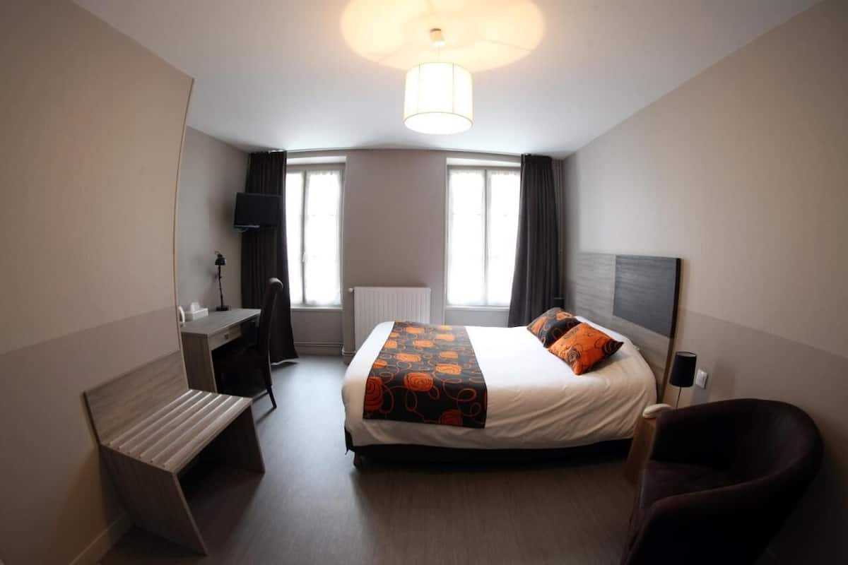 A hotel room with a bed, desk, chair, and a large window.