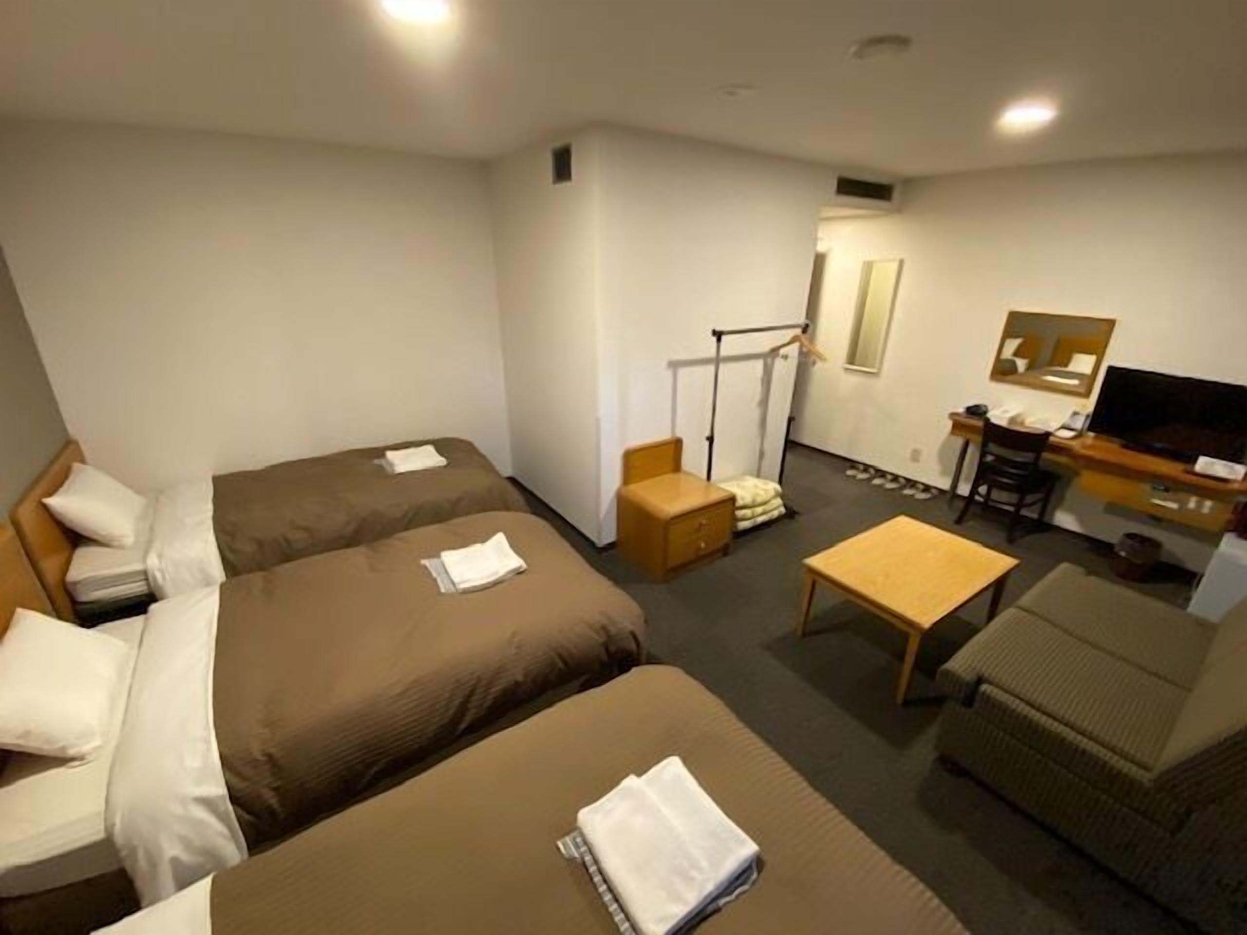 A hotel room with two beds, a desk, a television, and a small seating area.