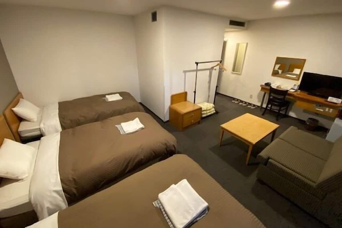 A hotel room with two beds, a desk, a television, and a small seating area.