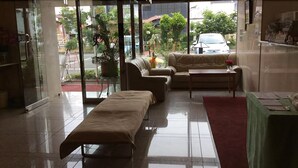 A spacious living area with a sofa, a bench, and a coffee table. There is a large window providing a view of the street and greenery outside. - Hotel New Yutaka (Izumisano)