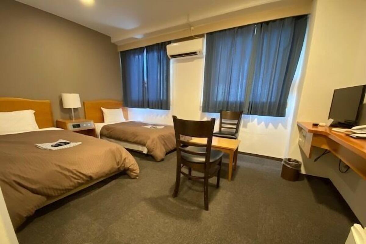 Ein Hotelzimmer mit zwei Betten, einem Schreibtisch, einem Stuhl, einer Klimaanlage und einem Fernseher.