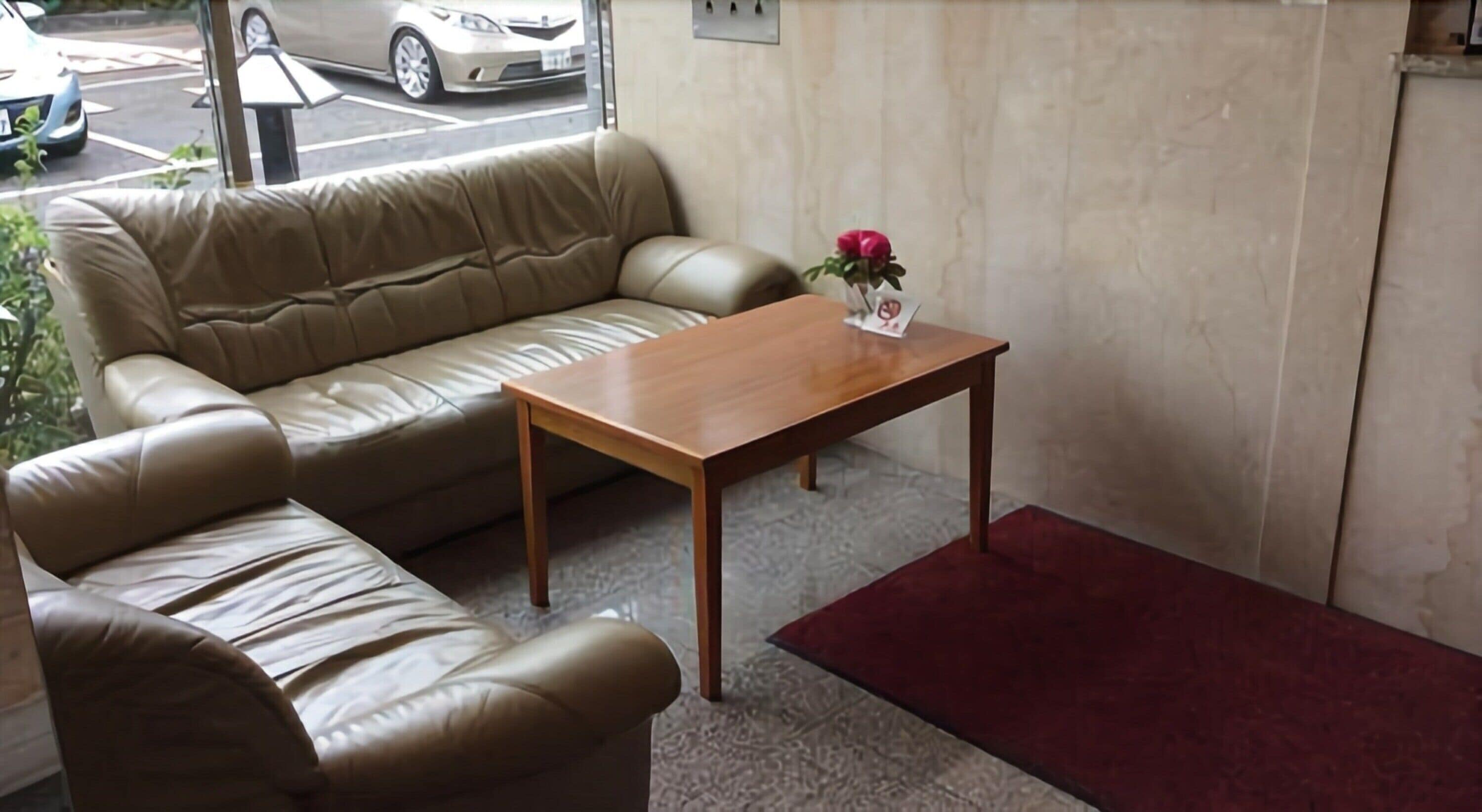 A room with a beige leather sofa, a wooden coffee table, and a red rug.