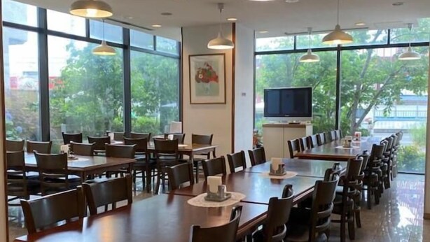 A conference room with multiple tables and chairs, large windows with a view of greenery, pendant lighting, and a flat-screen TV on a stand. - Hotel New Yutaka (Izumisano)