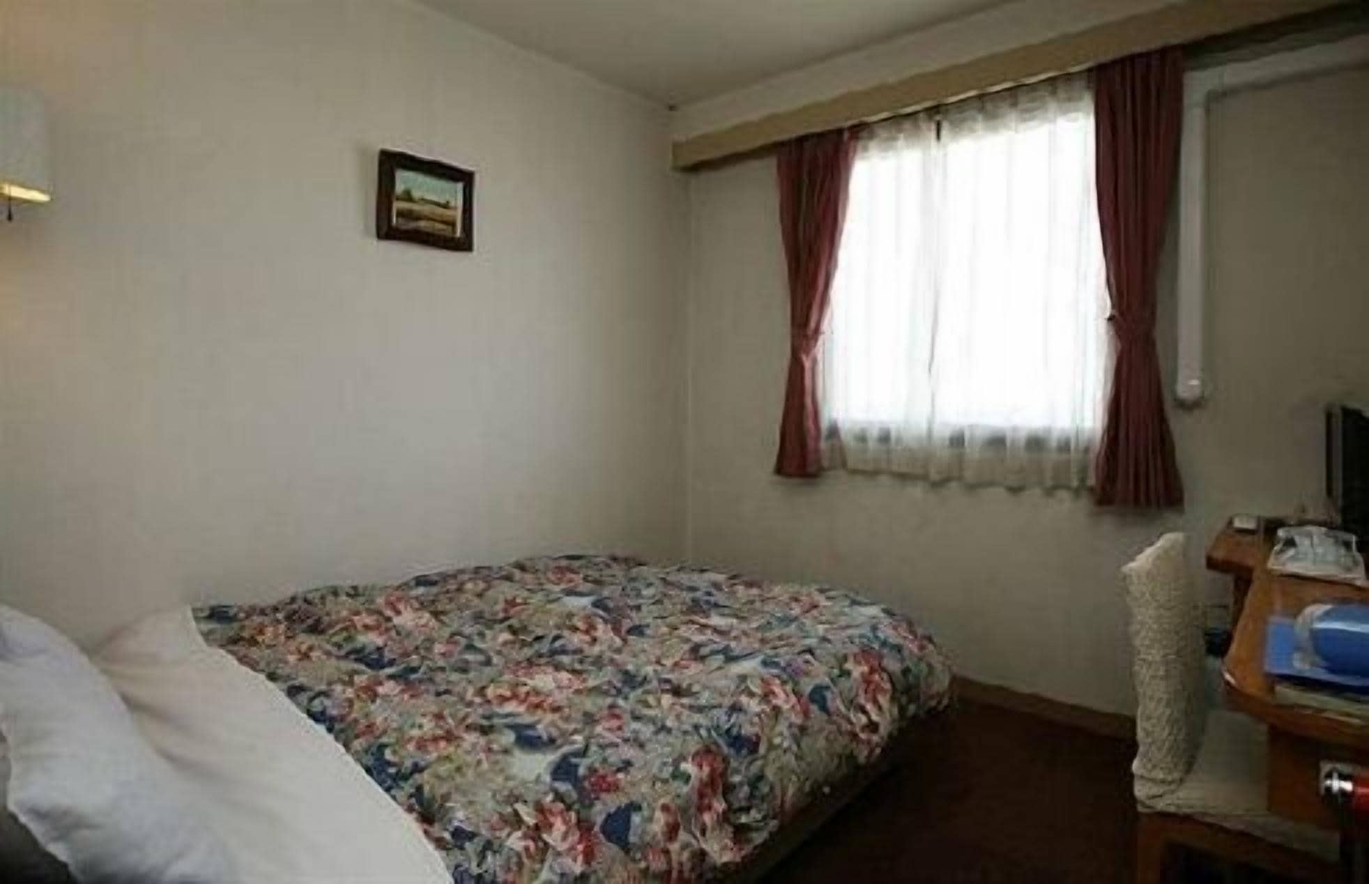A hotel room with a bed, a desk, and a window with curtains.