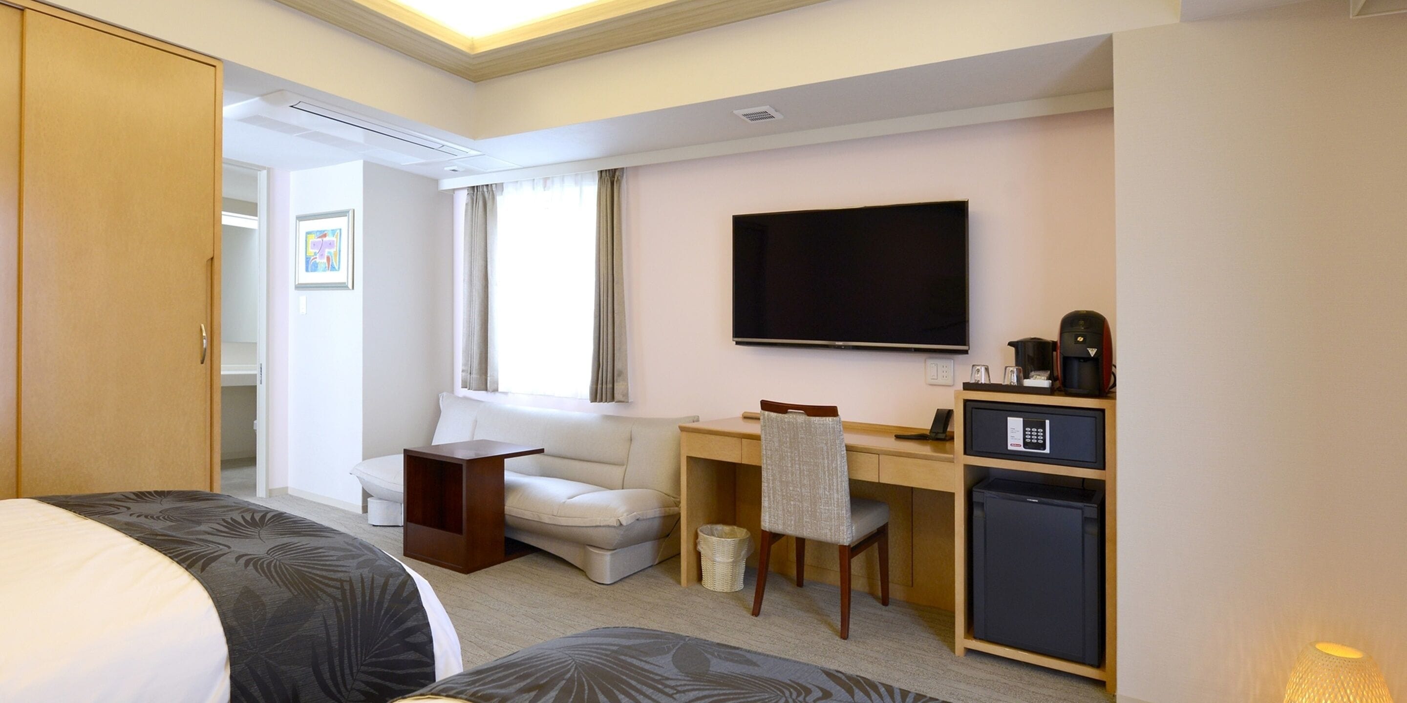 A hotel room with a bed, a desk, a chair, a TV, a mini-fridge, and a wardrobe.