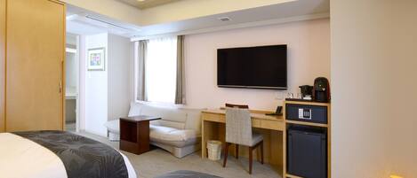 Habitación de hotel con cama, escritorio, silla, televisión, mini refrigerador y armario.
