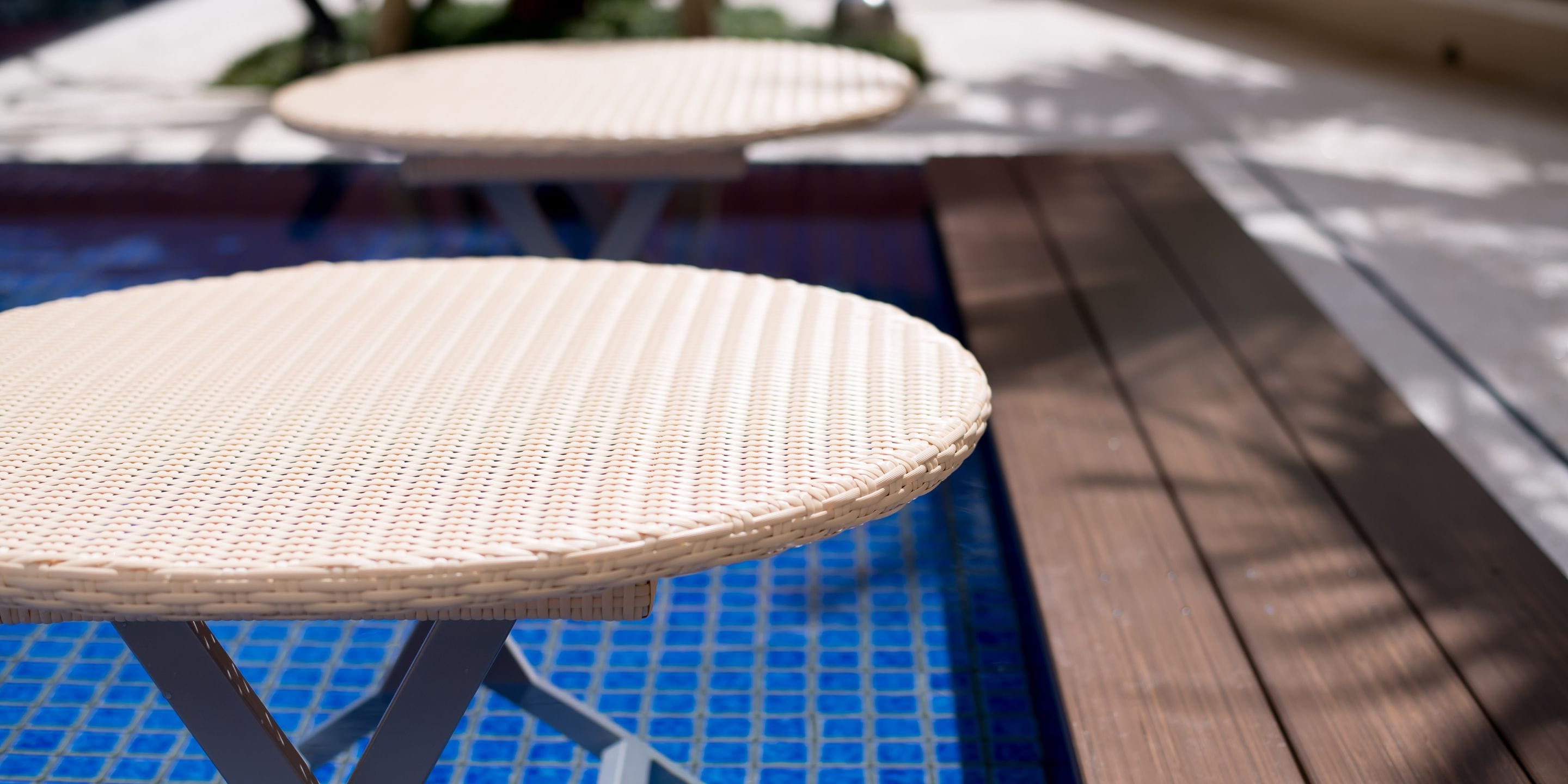 A poolside area with wicker tables and a wooden deck.