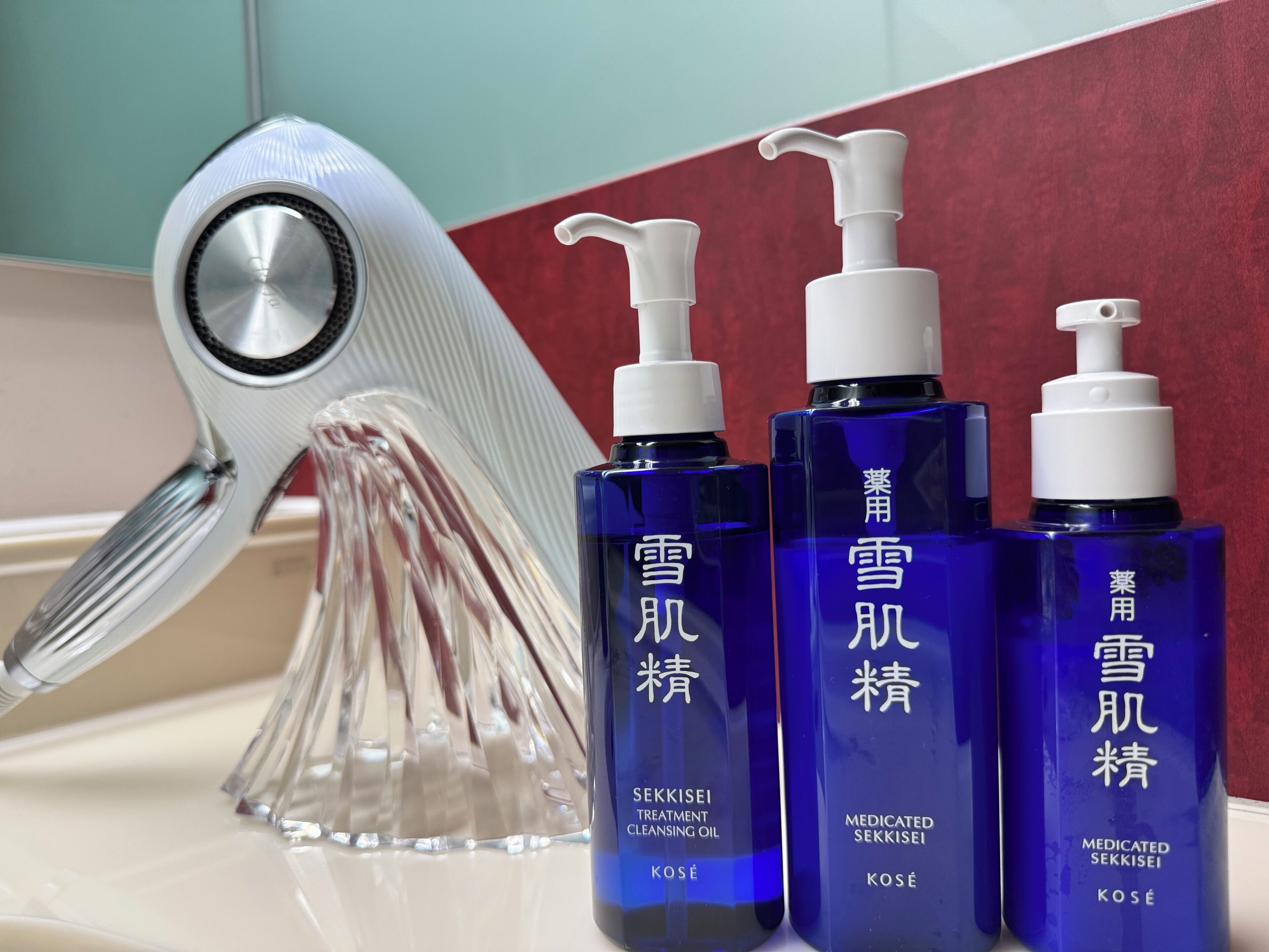 Three bottles of SEKKISEI treatment cleansing oil and a clear glass sculpture on a bathroom counter.